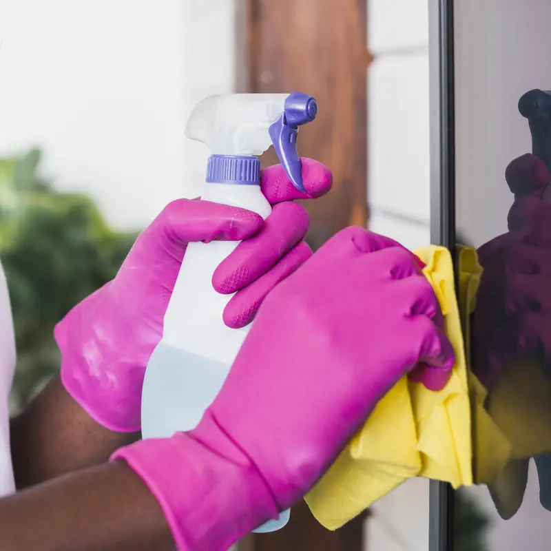 Close-up of gloved hands polishing glass with a spray bottle